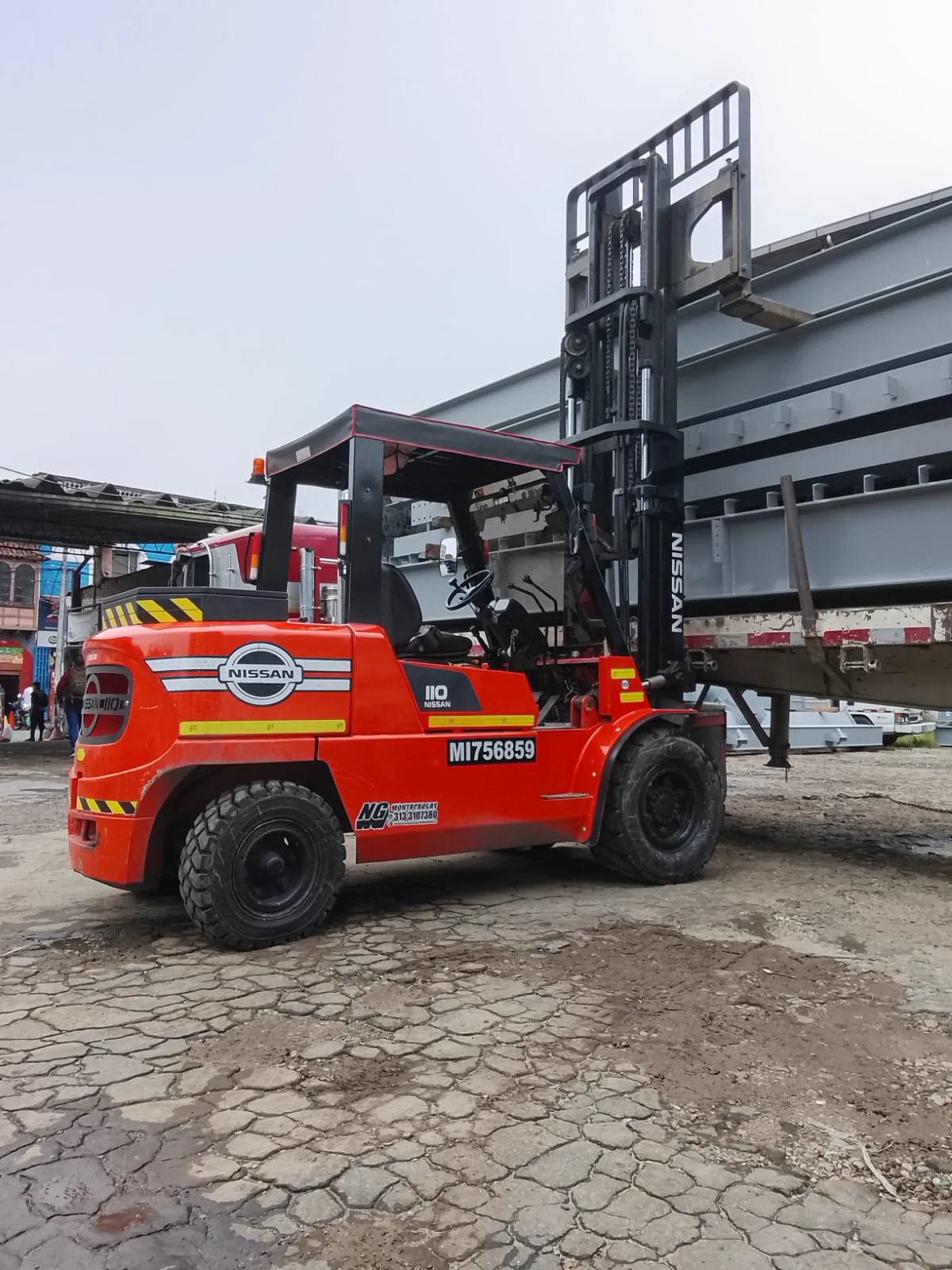 Montacargas Nissan rojo con operador experto elevando grandes estructuras metálicas de un camión en patio logístico.